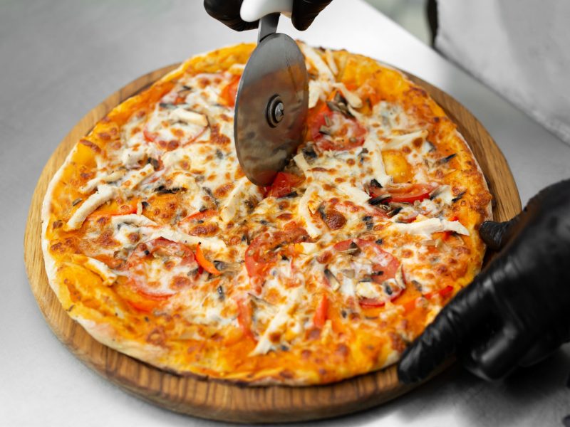 Closeup hand of chef cuts freshly prepared pizza slices at kitchen